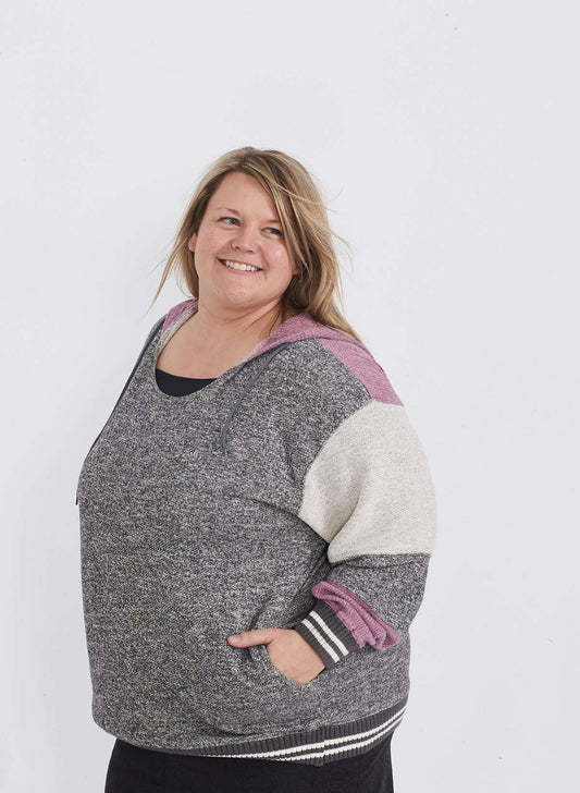 Plus size woman wearing a gray and purple hooded color block sweatshirt. It also has front pockets and banded wrist and waist.